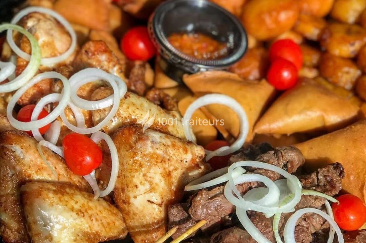 Assortiment de grillades, samoussas, légumes et sauce, garni d'oignons et tomates cerises.