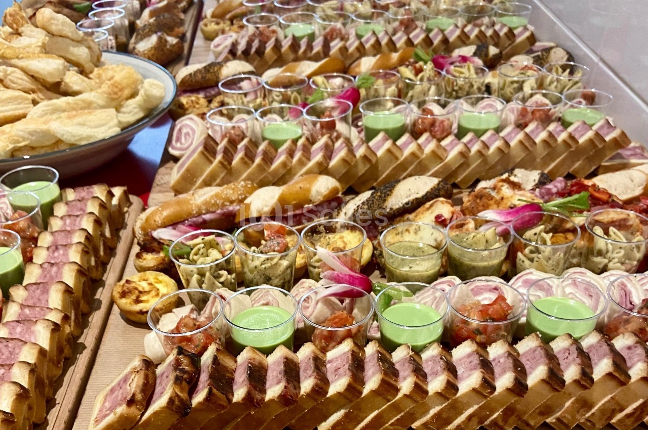 Plateau de buffet avec assortiments de sandwichs, verrines, quiches et feuilletés disposés en rangées.