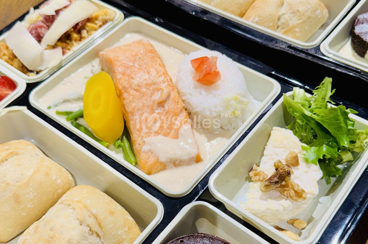 Plateau-repas avec saumon, riz, légumes, salade verte, fromage aux noix et pain, présenté dans des compartiments.