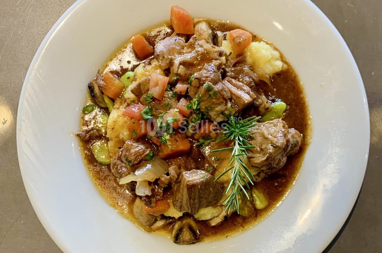 Assiette de ragoût de viande avec légumes, servi sur une purée de pommes de terre, garnie d'herbes fraîches.