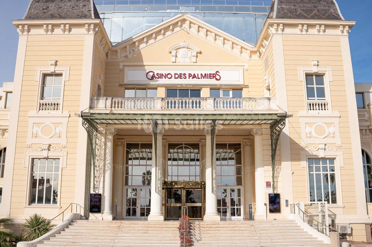 Façade d'un bâtiment historique beige avec une enseigne ’Casino des Palmiers’ et un escalier central.