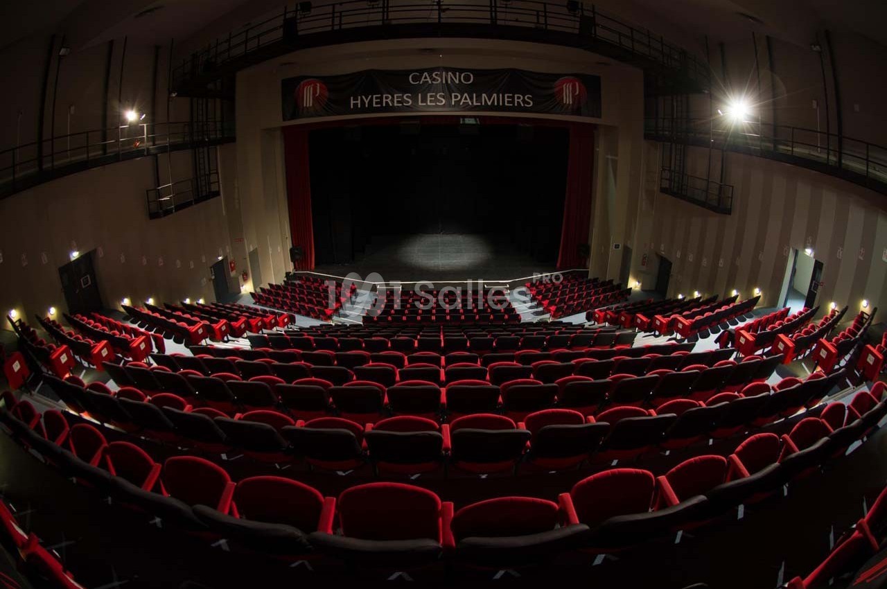 Salle de spectacle avec rangées de sièges rouges, scène éclairée et enseigne ’Casino Hyères Les Palmiers’.
