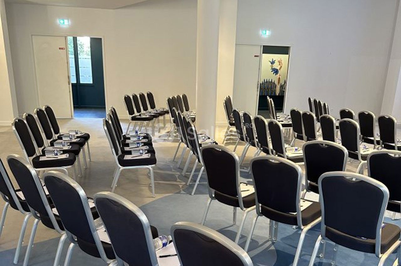 Salle de conférence avec des rangées de chaises noires alignées, disposées face à un espace vide.