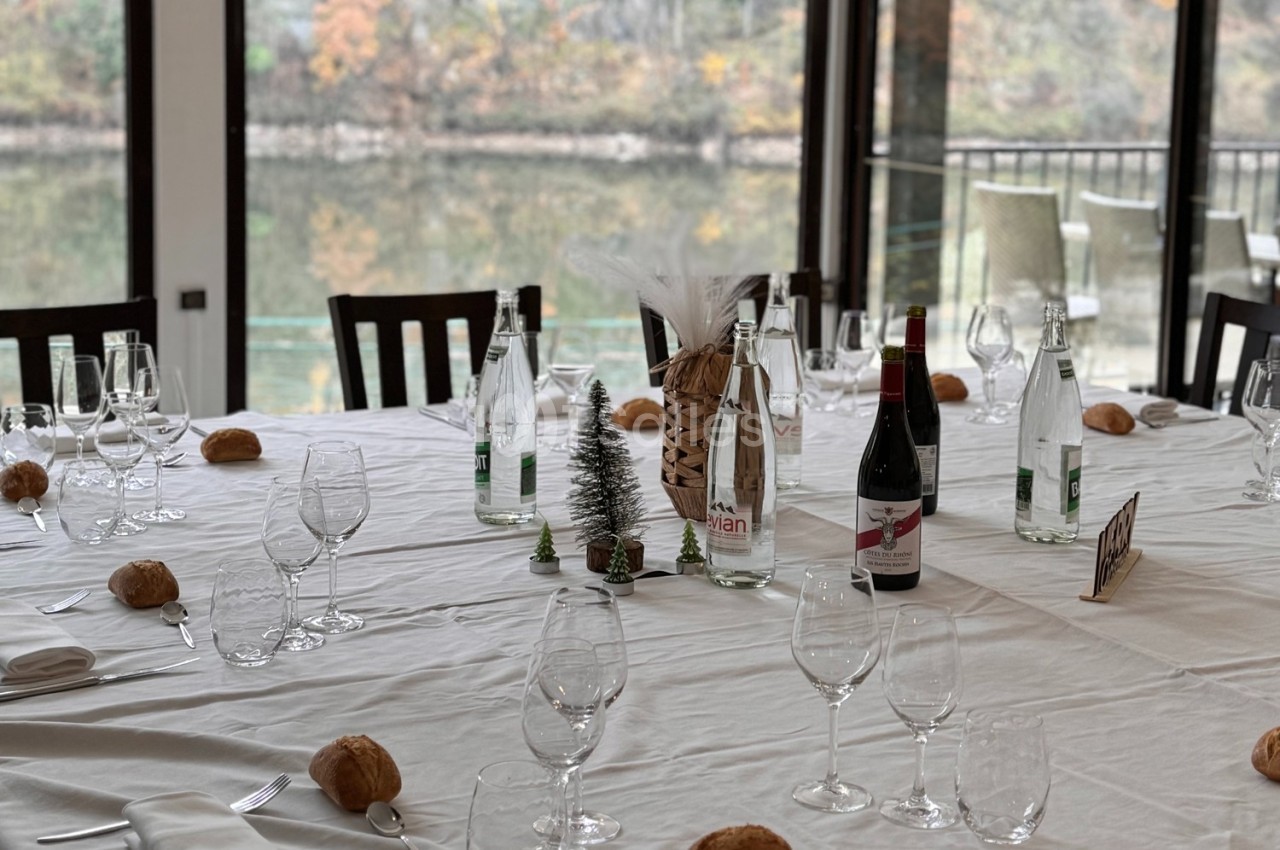 Table dressée avec nappes blanches, verres, bouteilles d'eau et de vin, petits pains et décorations miniatures.