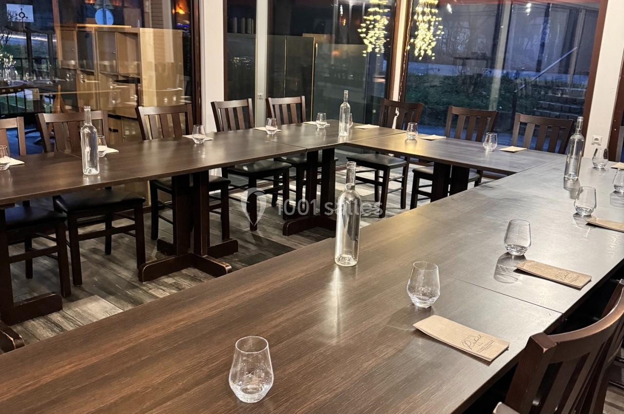 Salle de réunion avec tables en bois disposées en U, chaises, carafes d'eau et verres, éclairée par des lumières extérieures.