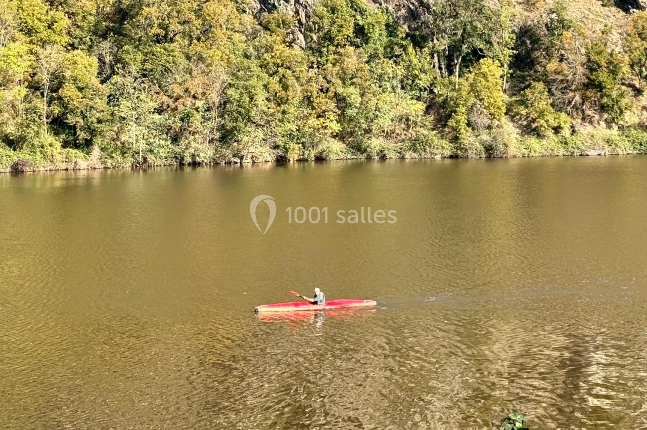 Un kayakiste pagaye sur une rivière calme entourée de végétation et de falaises verdoyantes.