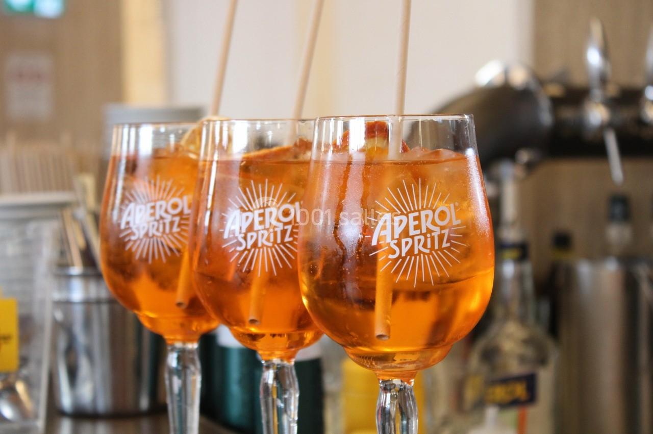 Trois verres d'Aperol Spritz garnis de glaçons et d'oranges, alignés sur un comptoir de bar.