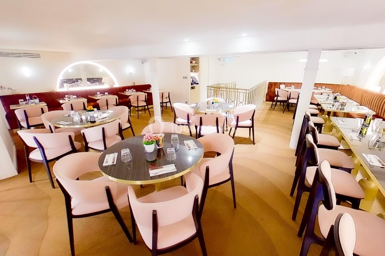 Salle de restaurant lumineuse avec tables rondes et rectangulaires, chaises rembourrées et décoration épurée.