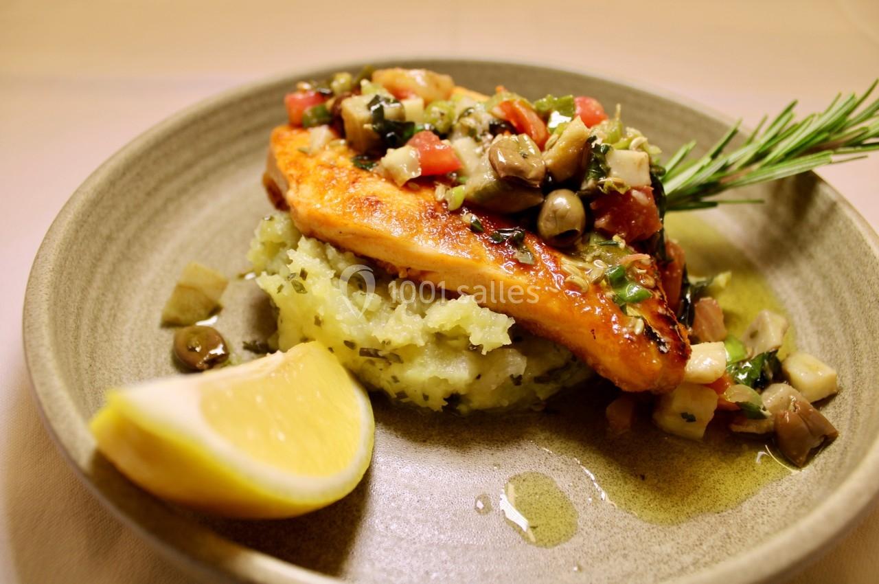 Filet de poisson grillé sur purée de pommes de terre, garni de légumes et herbes, avec un quartier de citron.