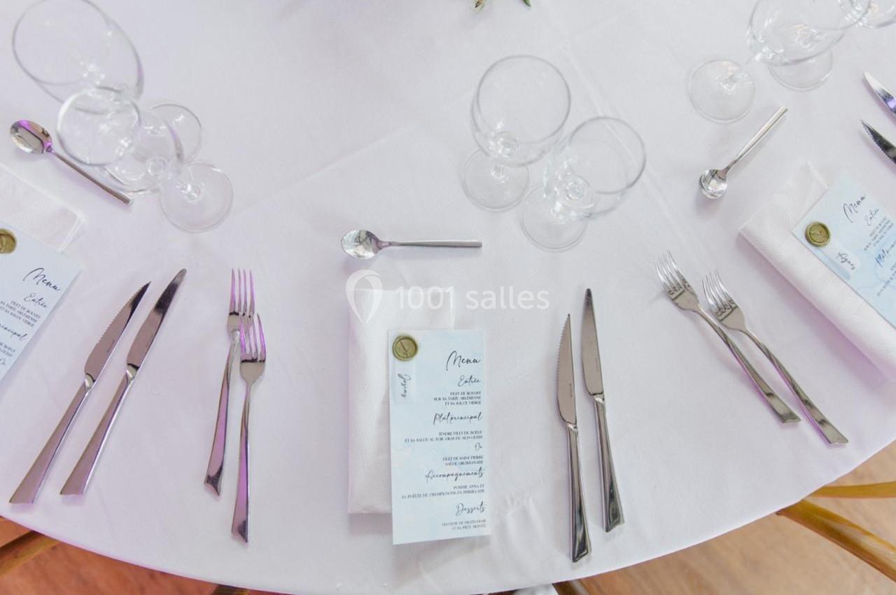 Table dressée avec nappes blanches, couverts, verres et menus disposés de manière élégante.