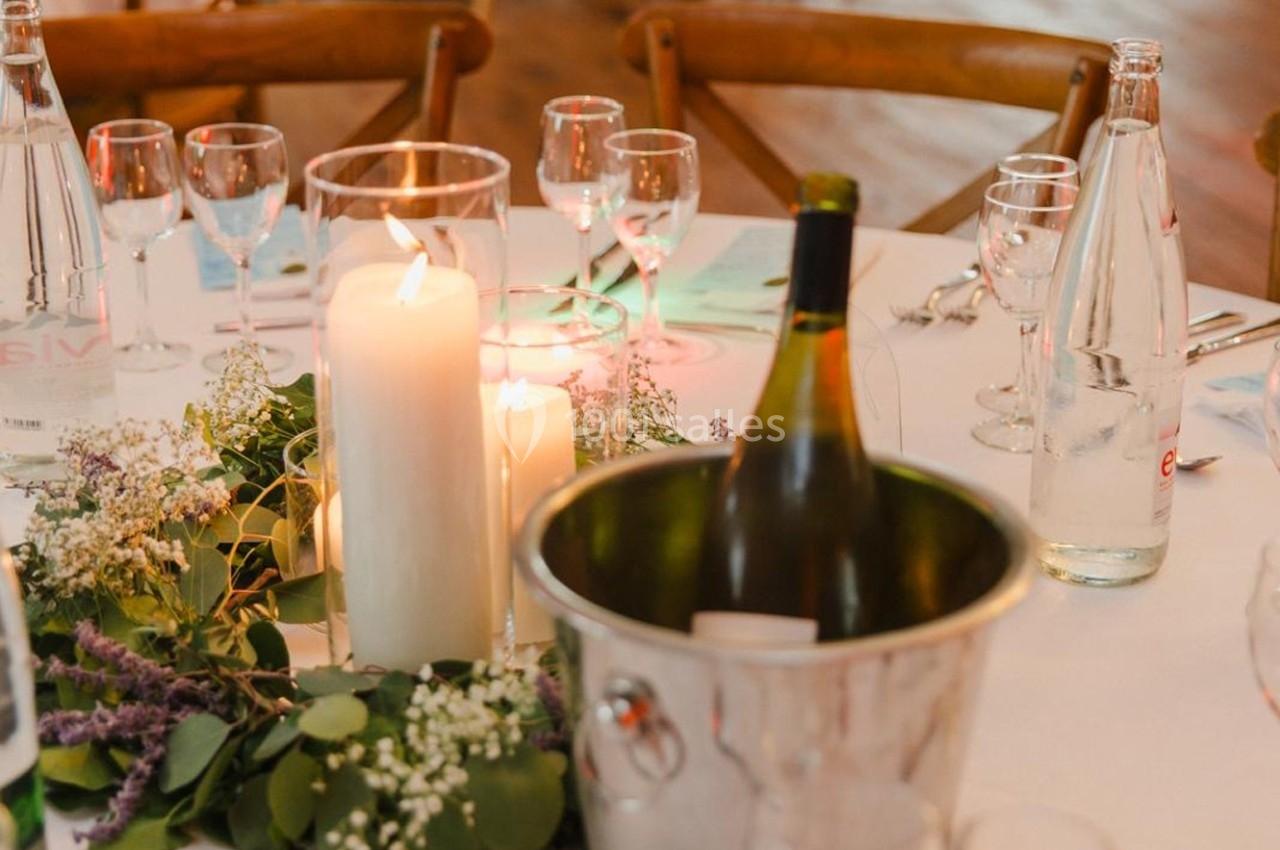 Table dressée avec des bougies allumées, des verres, une bouteille de vin dans un seau et une décoration florale.