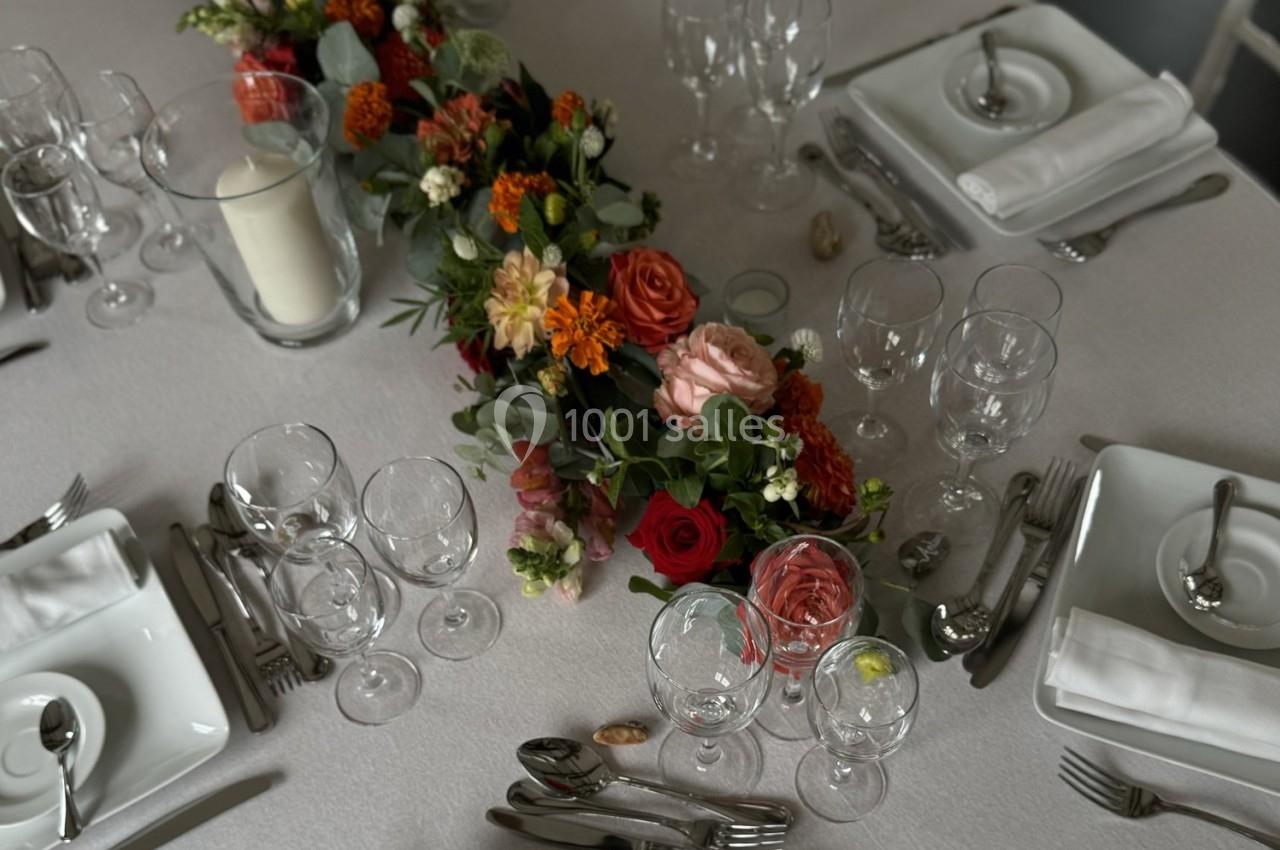 Table dressée avec une nappe blanche, décorée d'un centre de table floral coloré et entourée de vaisselle élégante.