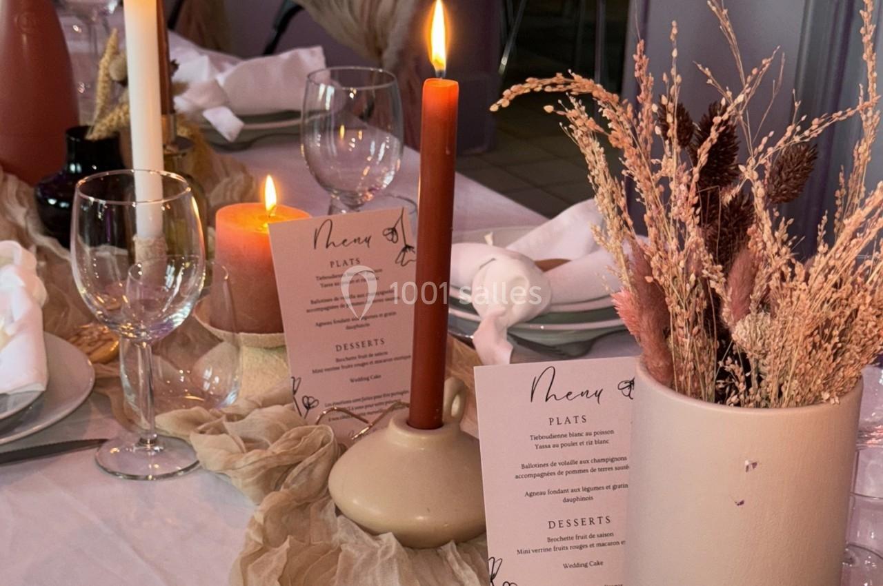 Table décorée avec des bougies, menus imprimés, vaisselle élégante et vase contenant des fleurs séchées.