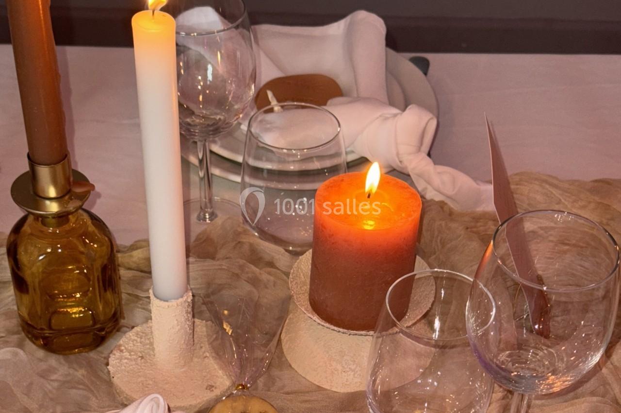 Bougies allumées sur une table décorée avec des verres, assiettes empilées et serviettes pliées.