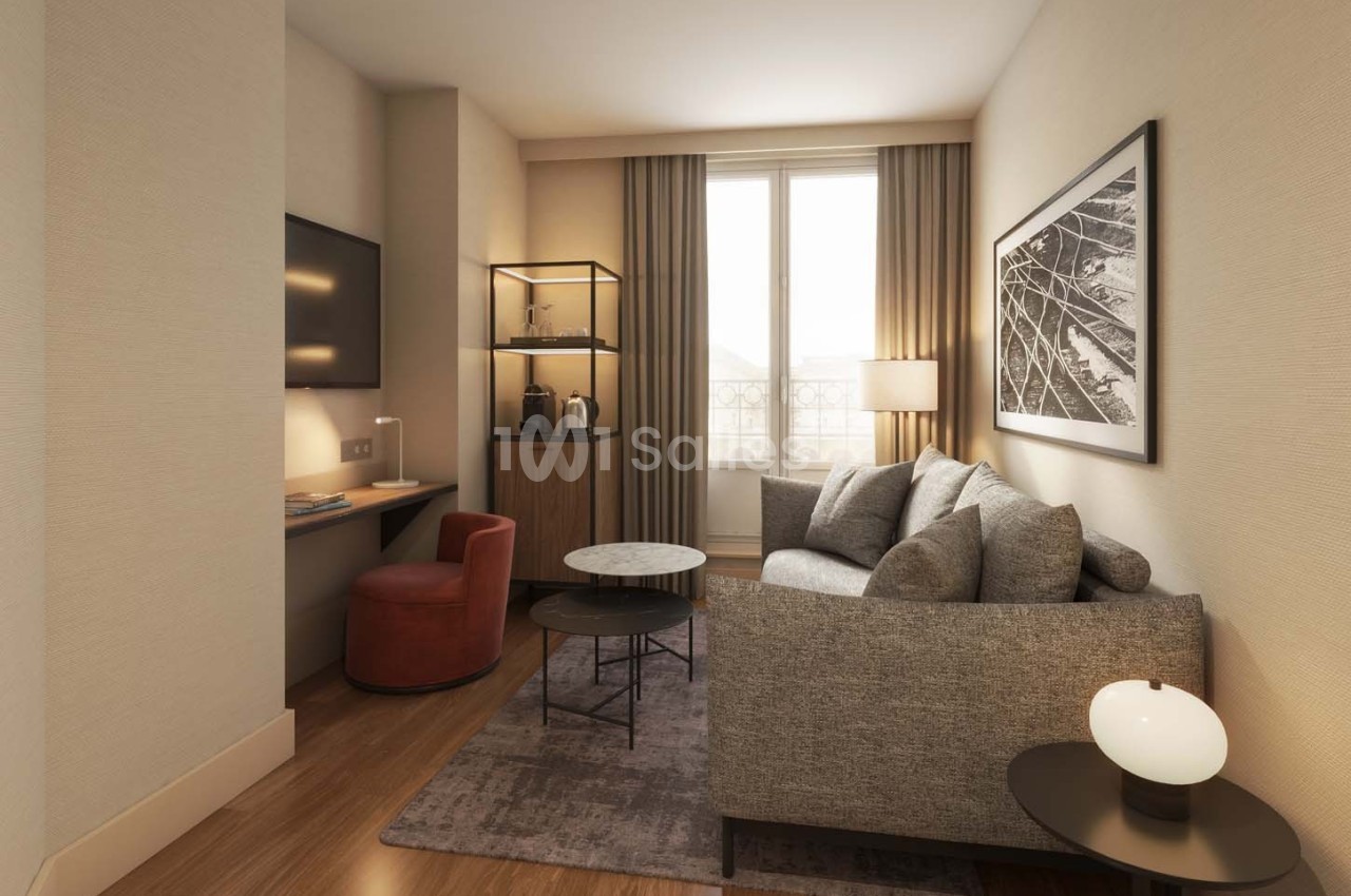 Salon moderne avec canapé gris, table basse, bureau avec chaise rouge, télévision murale et grande fenêtre avec rideaux.