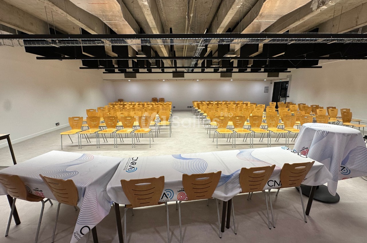 Salle de conférence avec des rangées de chaises jaunes alignées face à des tables recouvertes de nappes blanches.
