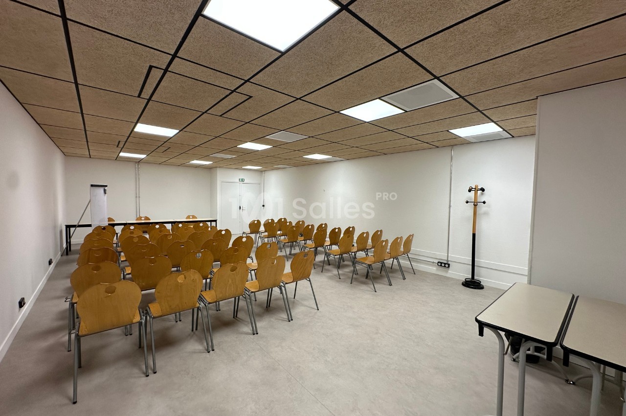 Salle de réunion lumineuse avec des rangées de chaises en bois disposées face à un mur blanc.