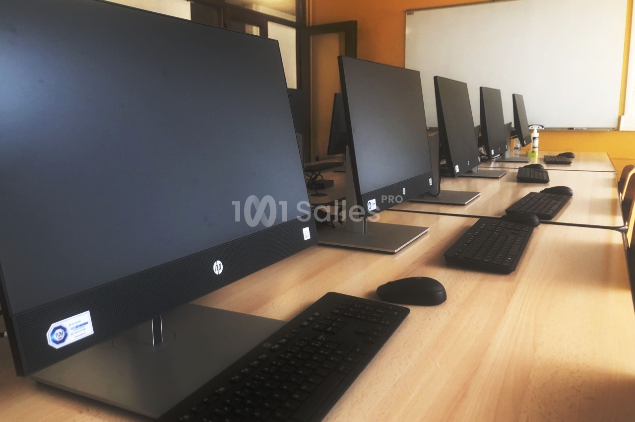 Ordinateurs alignés sur des bureaux en bois dans une salle équipée d'un tableau blanc.