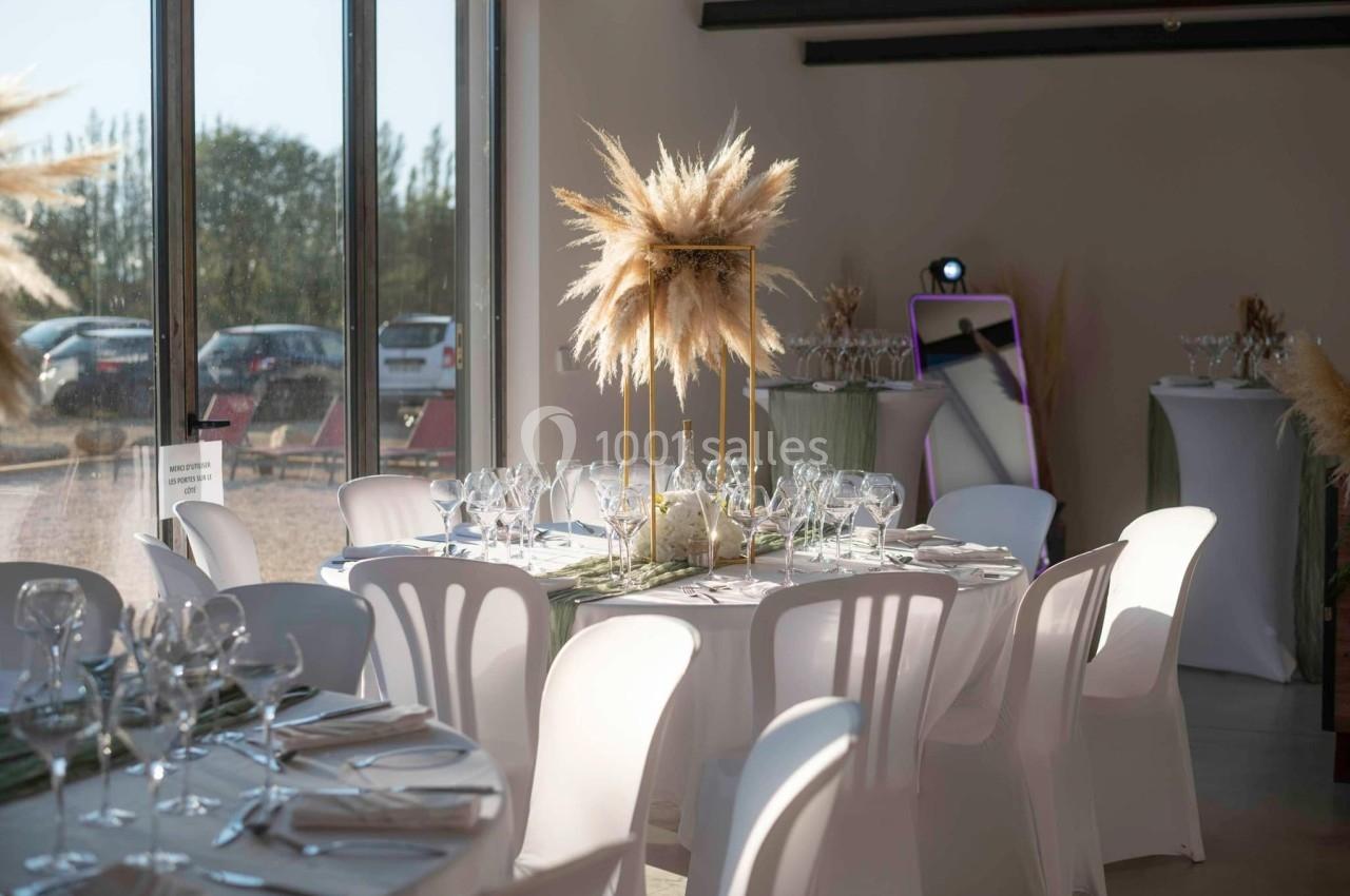 Salle de réception décorée avec des tables rondes, nappes blanches, chaises assorties et centre de table en pampas.