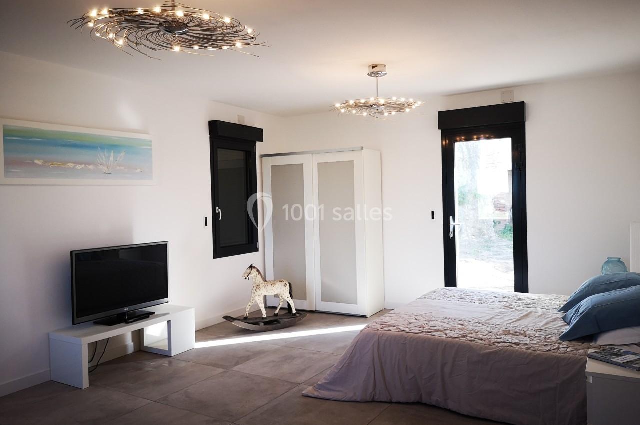 Chambre moderne avec lit double, armoire blanche, télévision, cheval à bascule et grandes fenêtres donnant sur l'extérieur.