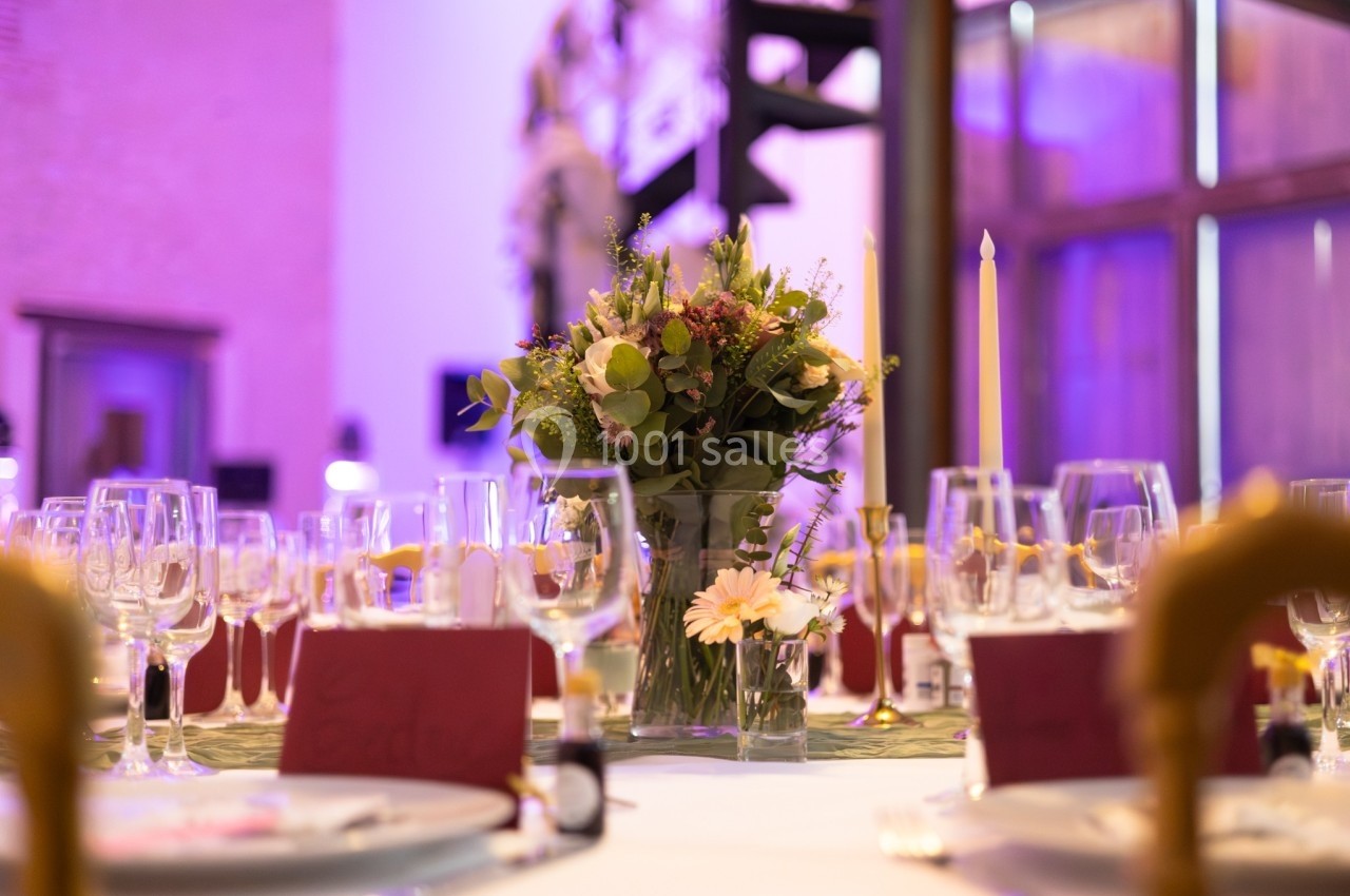 Centre de table floral entouré de verres et de couverts dans une salle éclairée par des lumières violettes.