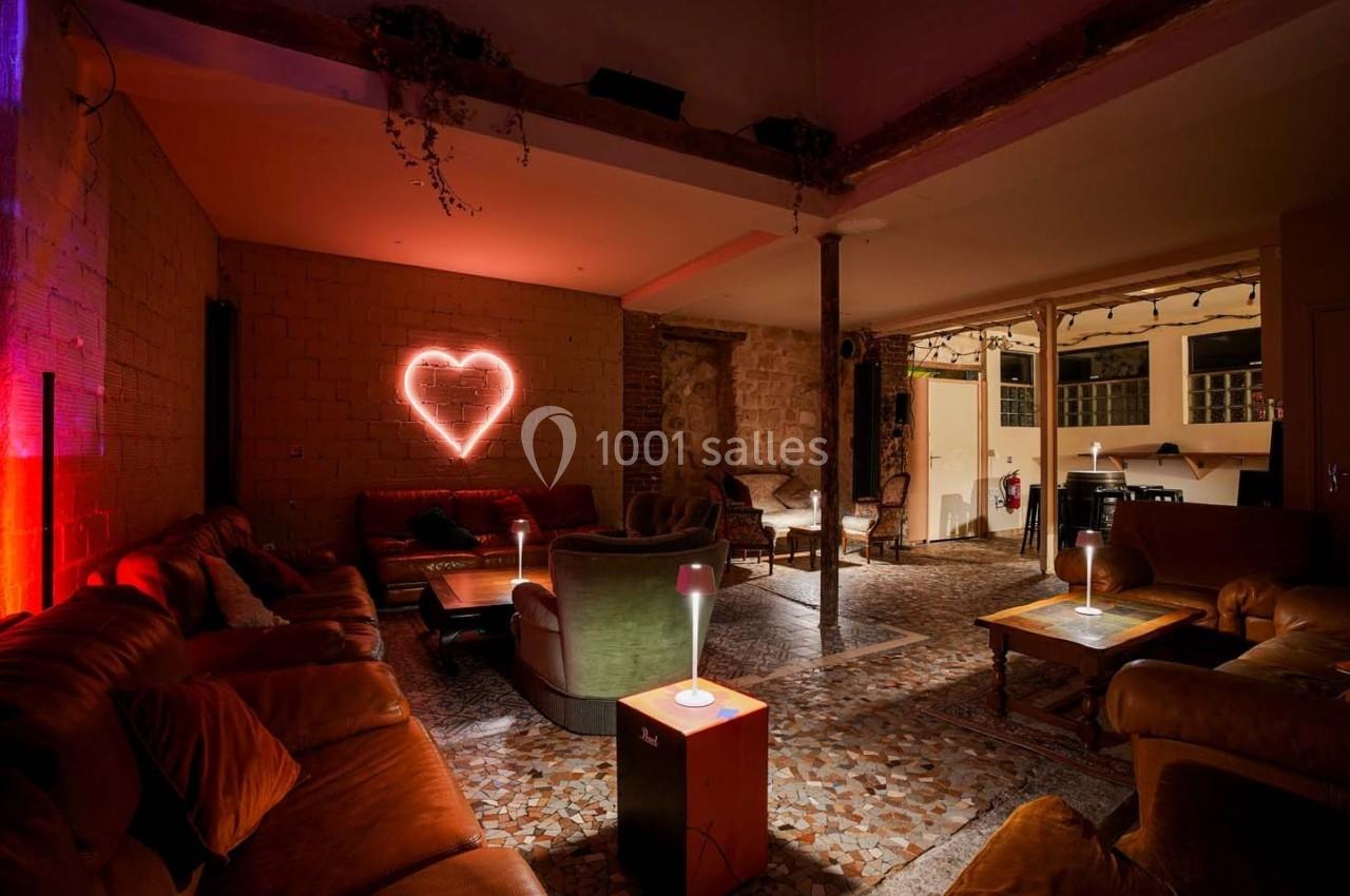 Salon cosy avec canapés en cuir, éclairage tamisé et cœur lumineux rouge au mur en briques.