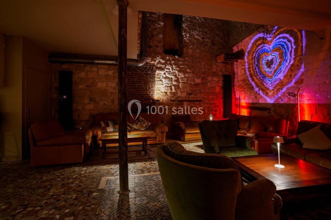Salle cosy avec murs en pierre, fauteuils, éclairage tamisé et projection lumineuse en forme de cœur.