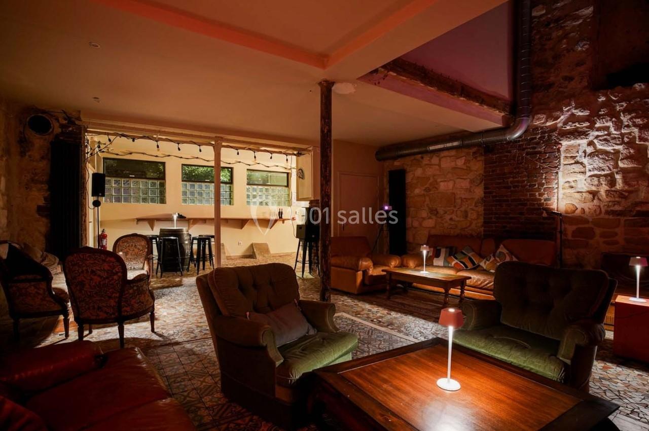 Espace intérieur chaleureux avec fauteuils, tables basses, murs en pierre et éclairage tamisé.