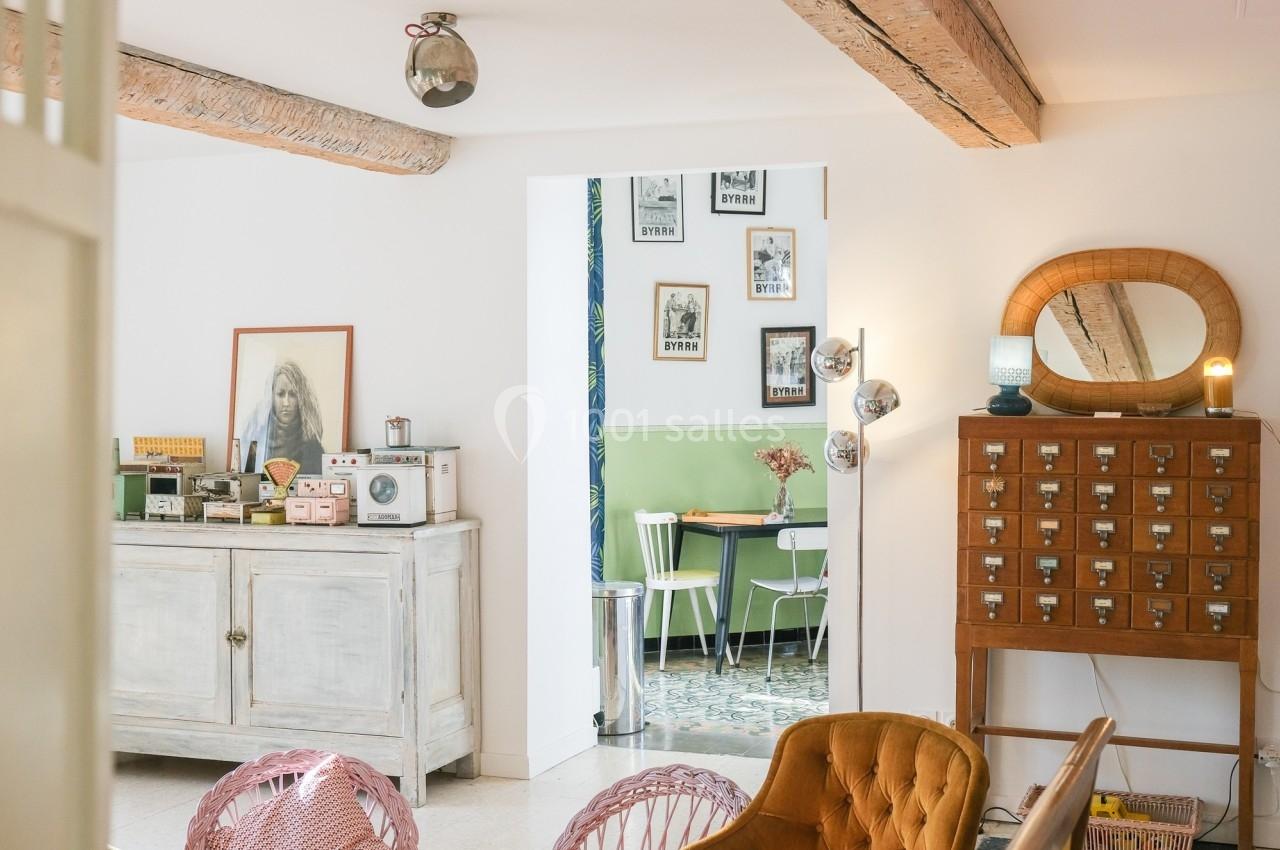 Intérieur lumineux avec meubles vintage, affiches encadrées au mur et vue sur une salle à manger aux tons verts.