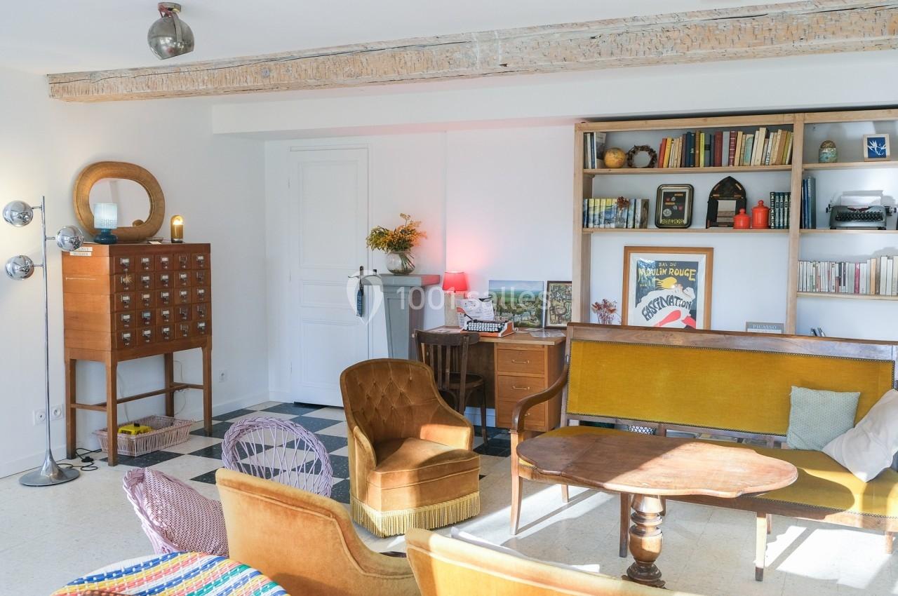 Salon lumineux avec mobilier vintage, étagères remplies de livres, poutres apparentes et décoration rétro.