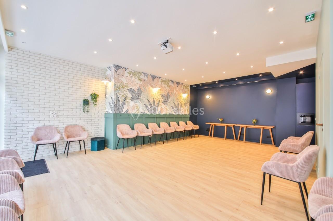 Salle lumineuse avec des chaises roses, murs décorés de motifs végétaux et un sol en bois clair.