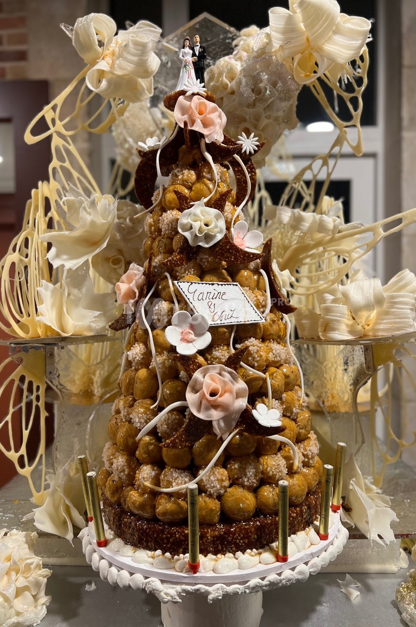 Pièce montée en choux décorée de fleurs en sucre, avec figurines de mariage au sommet et détails en caramel filé.