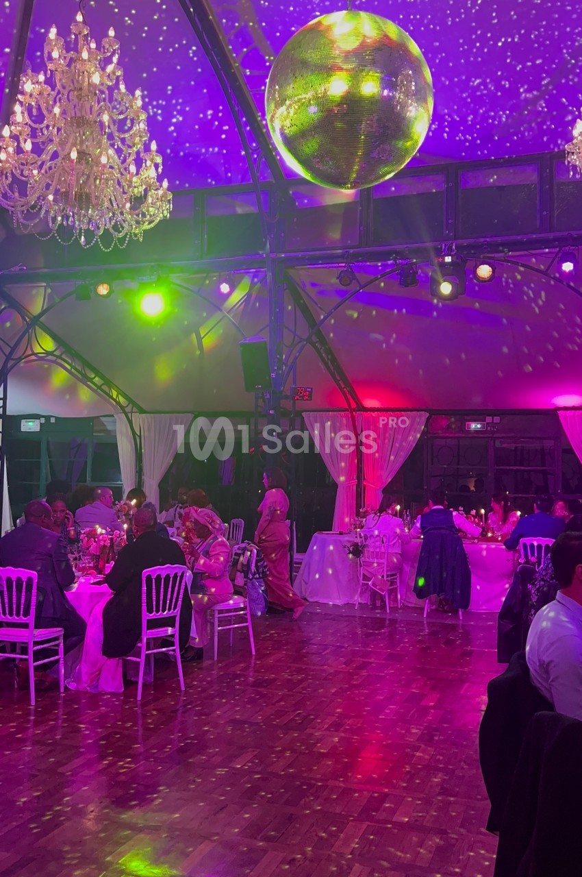 Salle de réception illuminée avec des invités assis à des tables décorées, sous une boule à facettes et des lustres.