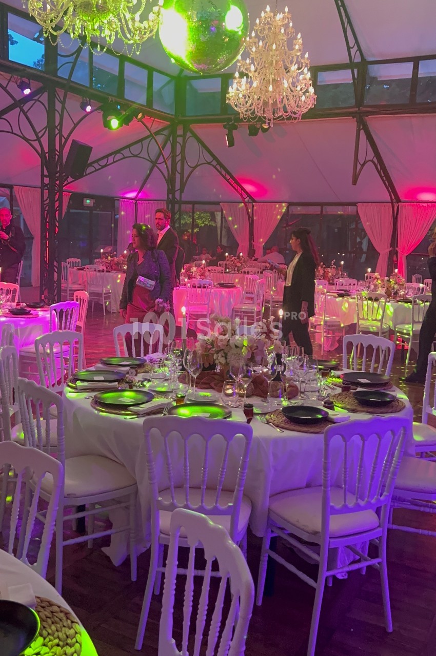 Salle de réception décorée avec des tables dressées, des chandeliers suspendus et un éclairage coloré.