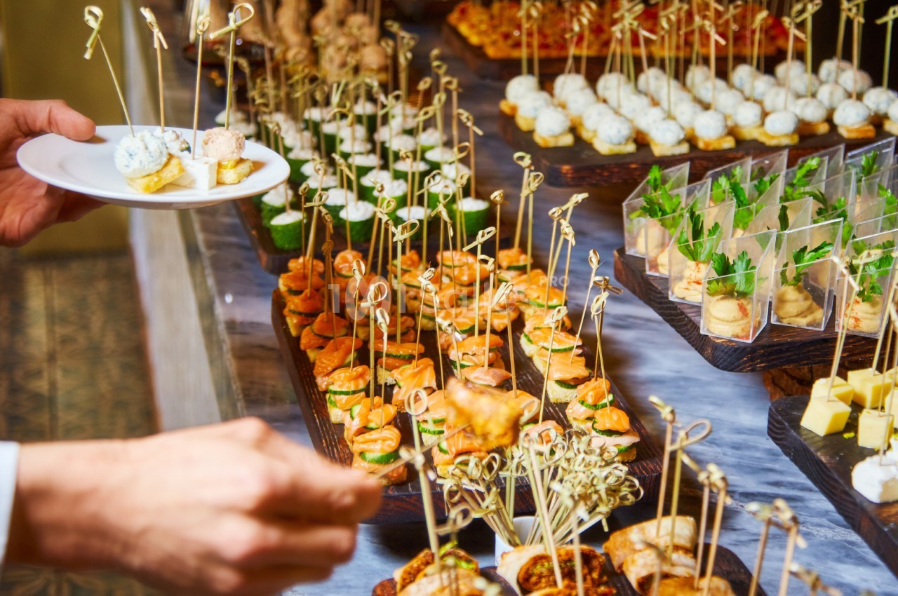 Plateau de bouchées apéritives variées présentées sur des brochettes, avec une personne servant un plat.