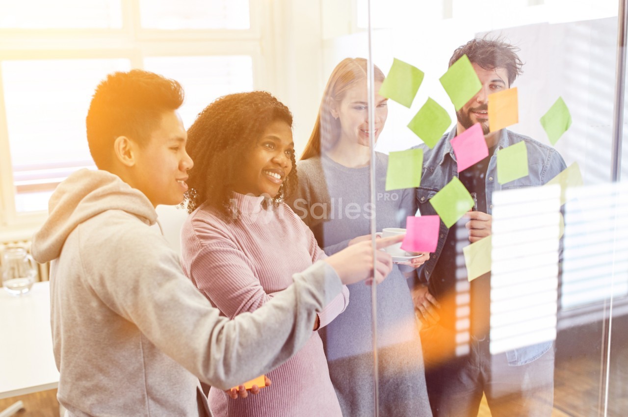 Des personnes collaborent autour d'un tableau en verre avec des notes autocollantes colorées dans un bureau lumineux.