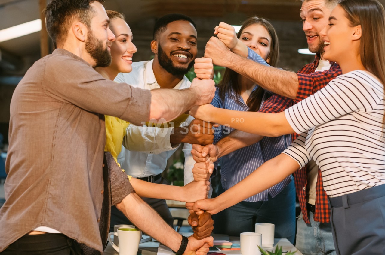 Un groupe de personnes souriantes se tient les mains en cercle dans un espace de travail collaboratif.