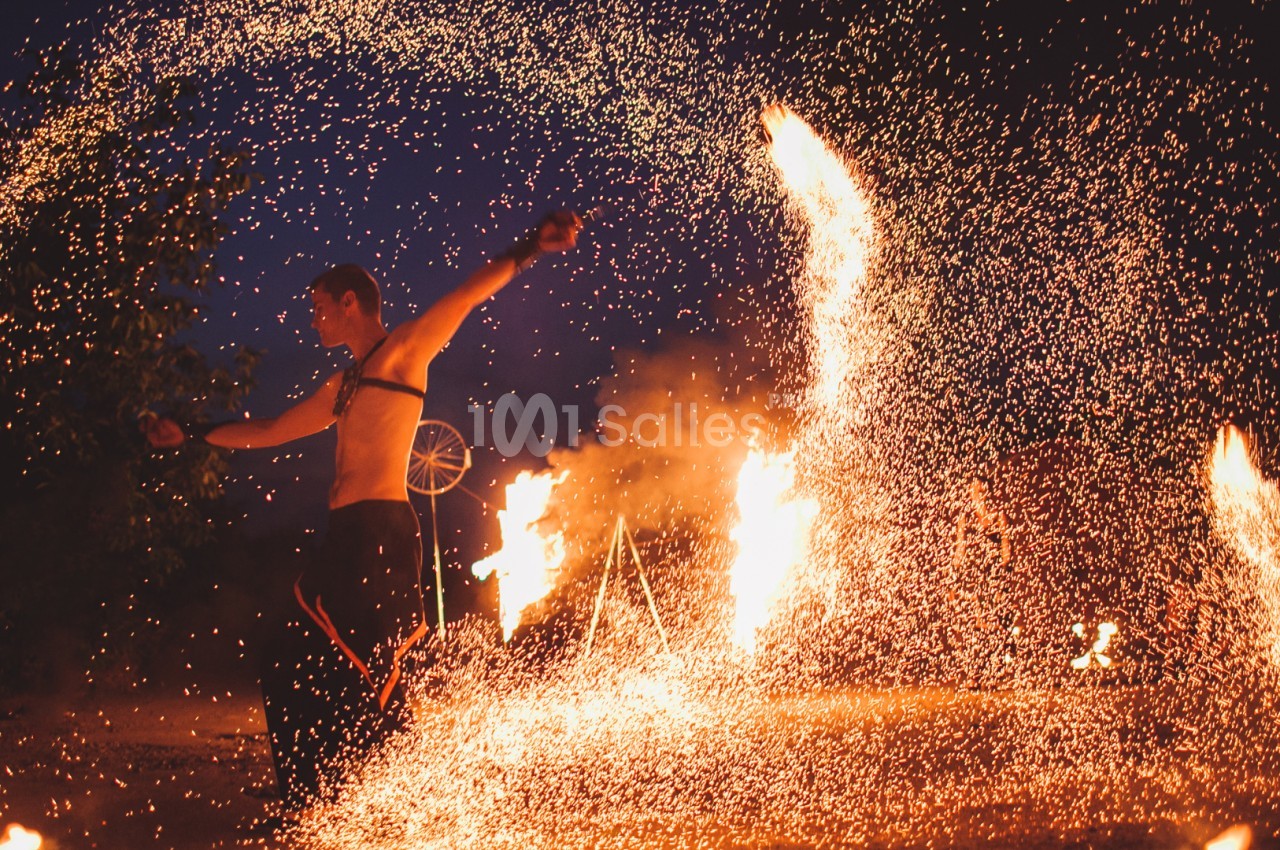 Un artiste jongle avec des torches enflammées, entouré d'étincelles, dans un décor nocturne.