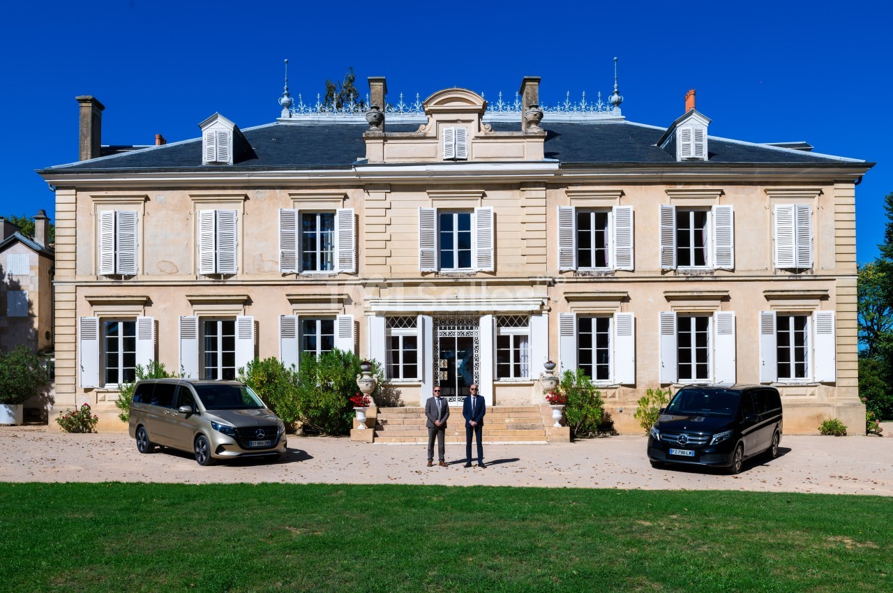Façade d'un grand bâtiment de style classique avec deux véhicules noirs stationnés devant et deux personnes debout.