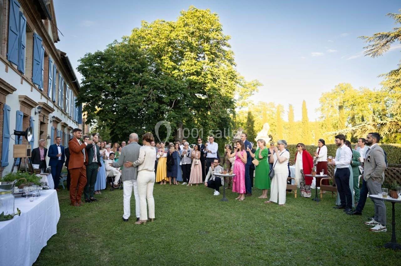 Groupe de personnes rassemblées dans un jardin lors d'une réception, avec un couple au centre face aux invités.