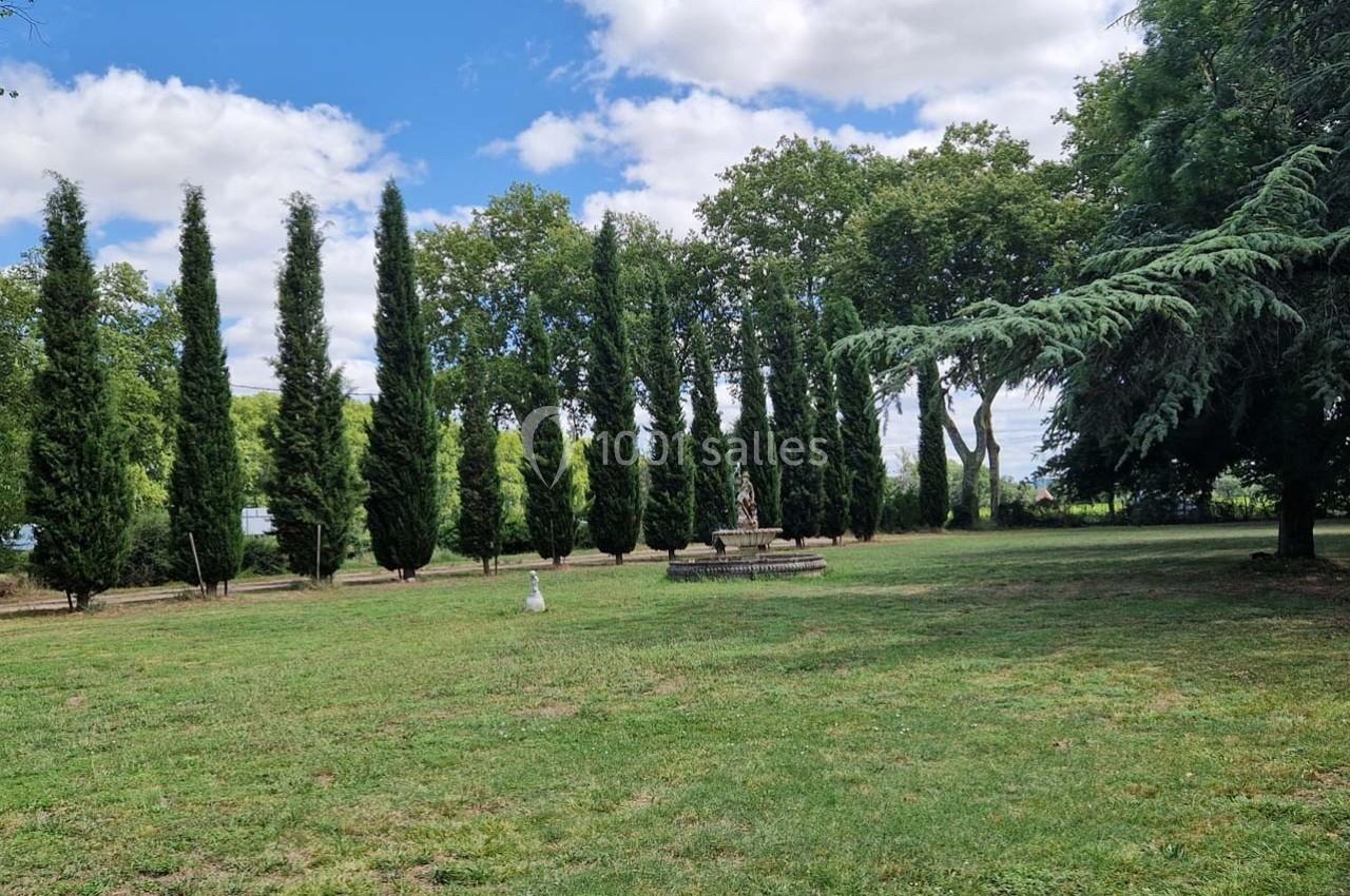 Alignement d'arbres et statue centrale dans un parc verdoyant sous un ciel partiellement nuageux.