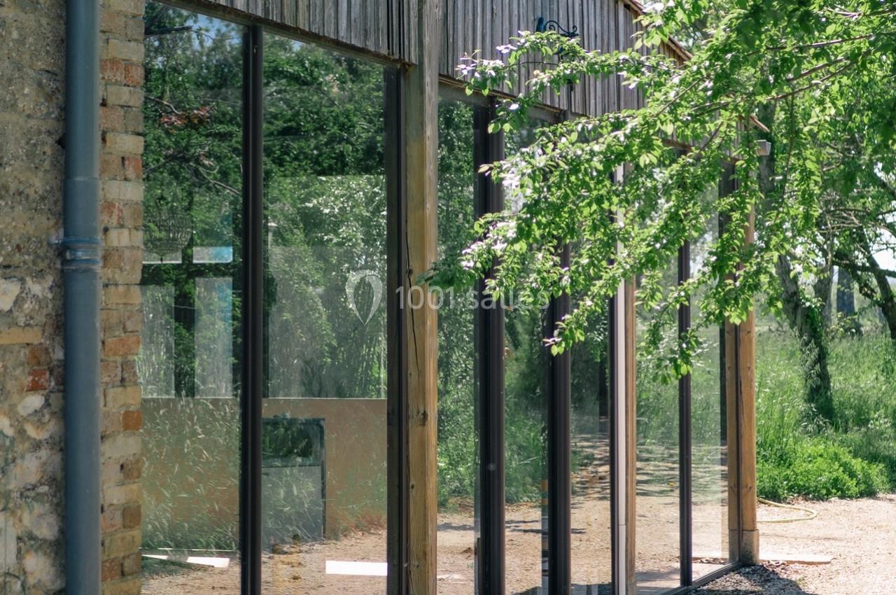 Façade vitrée d'un bâtiment en bois et pierre, entourée de végétation et baignée de lumière naturelle.