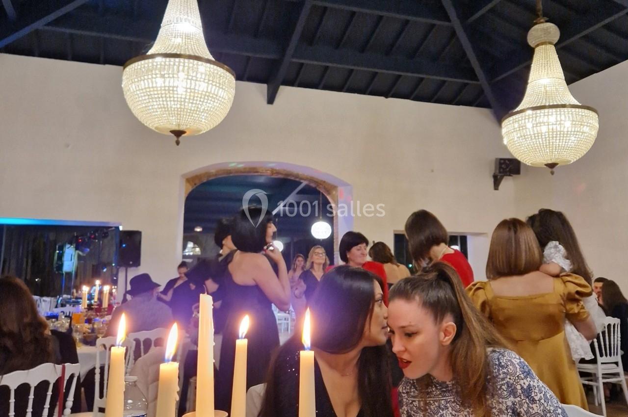 Des personnes discutent et dansent dans une salle éclairée par des lustres et des bougies sur une table au premier plan.