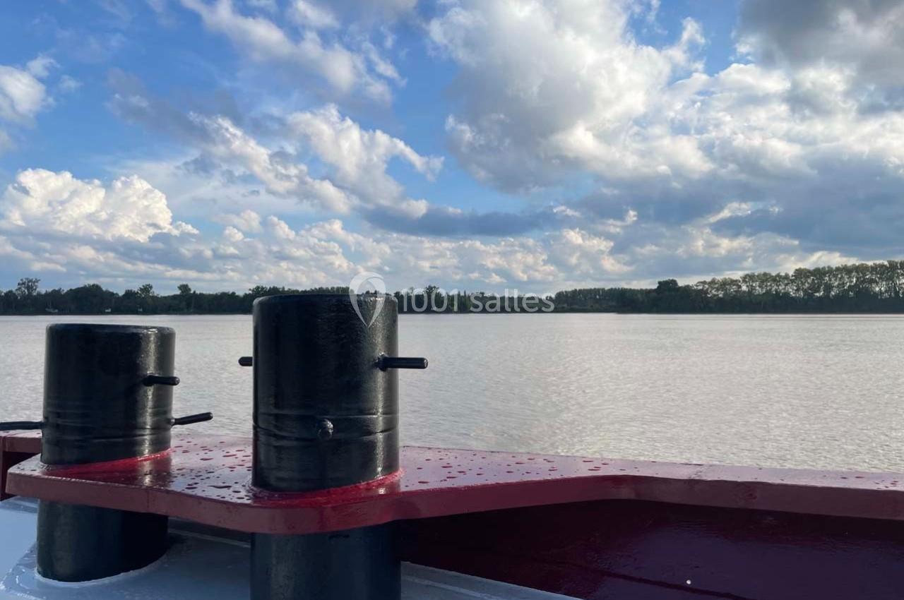 Vue d'un fleuve calme sous un ciel partiellement nuageux, avec des éléments d'un bateau au premier plan.