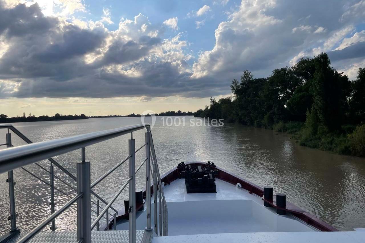 Vue depuis le pont avant d'un bateau naviguant sur une rivière bordée d'arbres, sous un ciel partiellement nuageux.