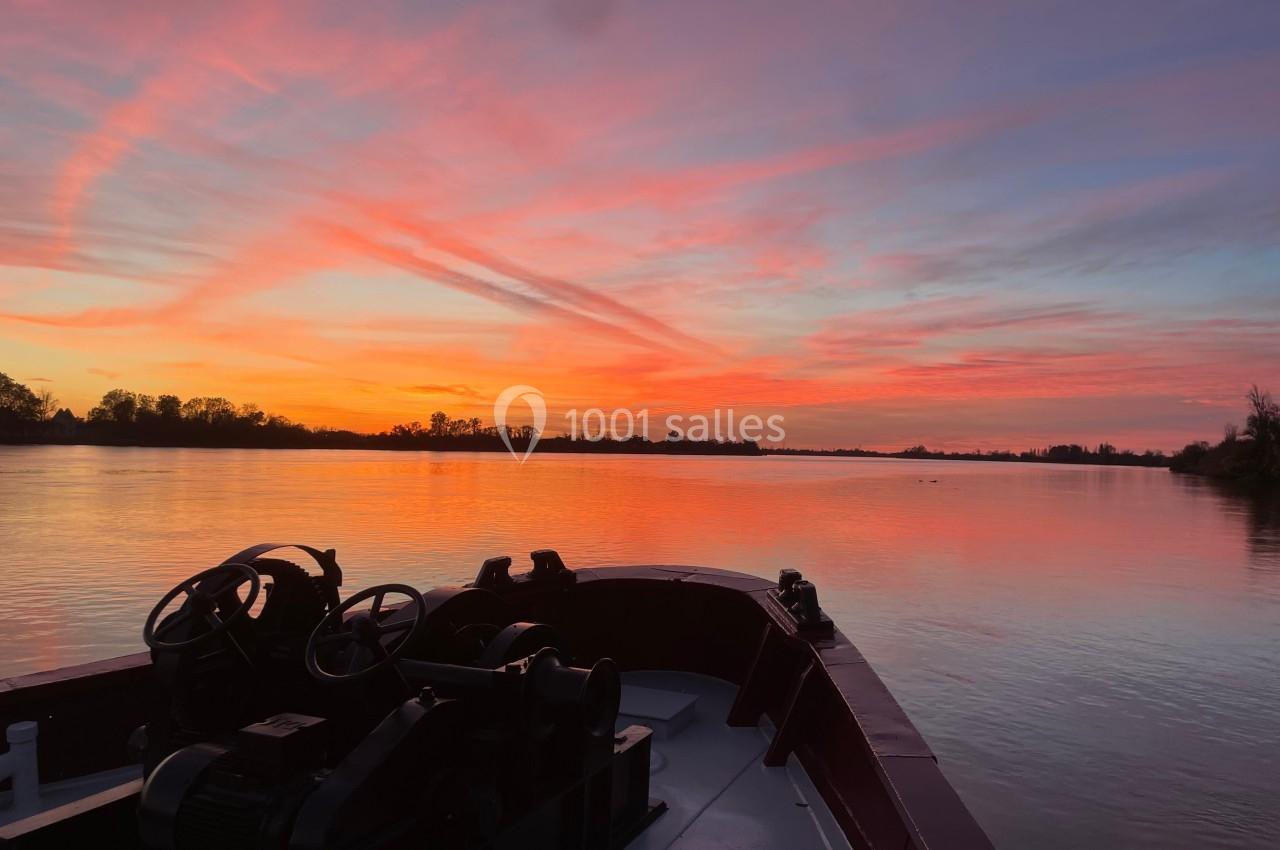 Coucher de soleil aux teintes roses et orangées reflété sur une rivière, vu depuis un bateau.
