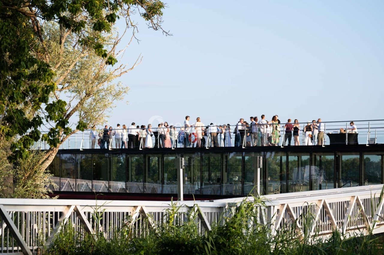Des personnes rassemblées sur une passerelle surélevée en plein air, entourée de végétation et d'arbres.