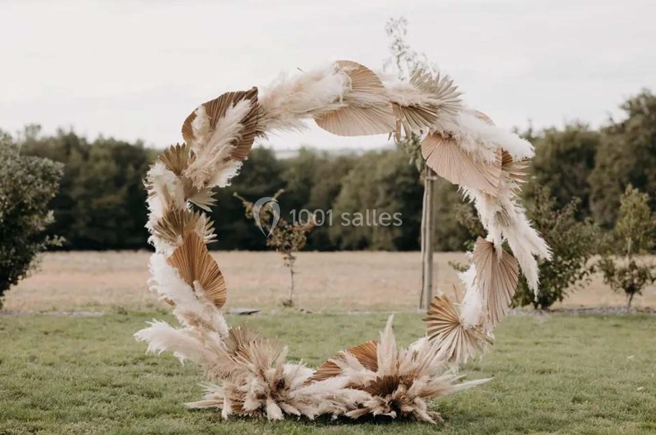 Cercle décoratif en feuilles séchées et pampas, installé sur une pelouse avec des arbres en arrière-plan.