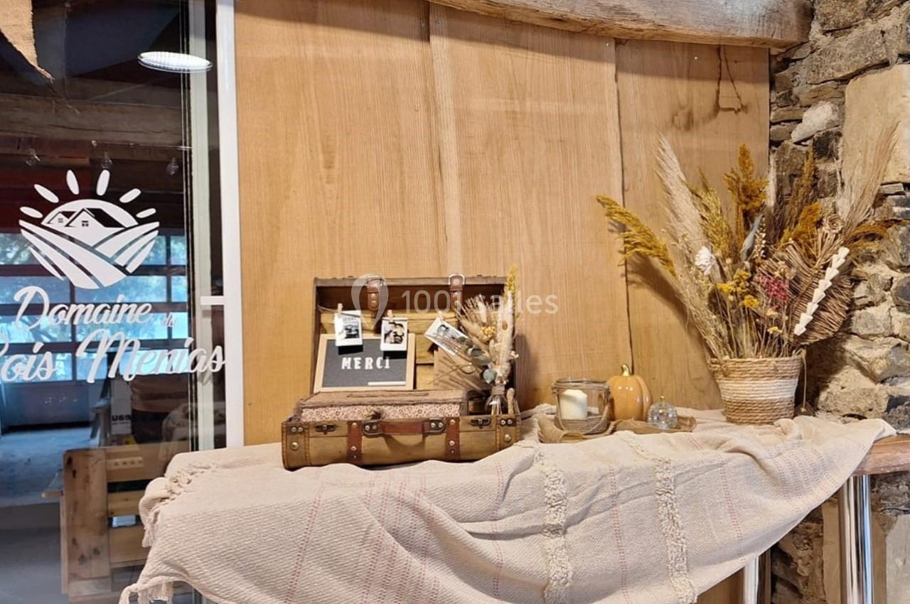 Décoration rustique avec valise vintage, fleurs séchées, bougie et citrouille sur une table en tissu beige.