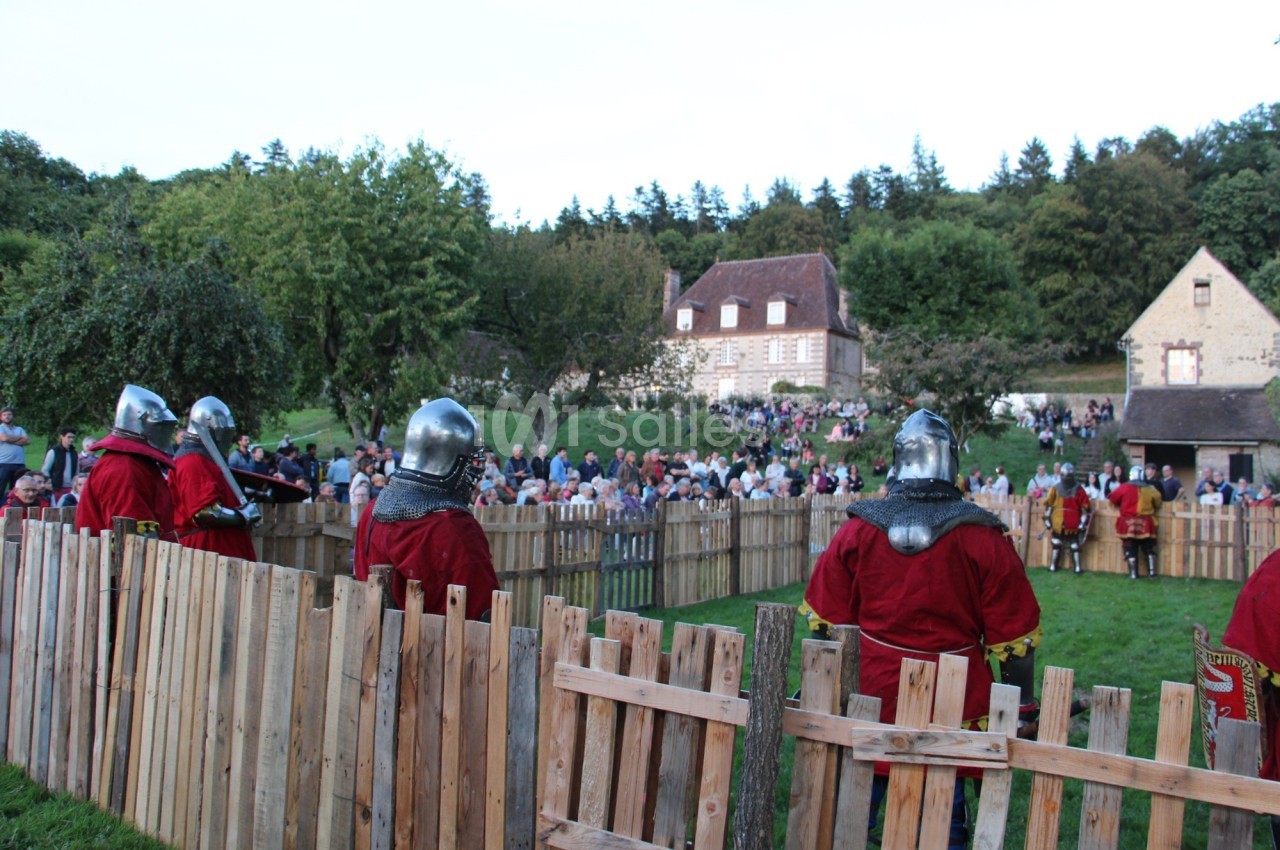 Des chevaliers en armure participent à une reconstitution médiévale devant un public rassemblé en plein air.